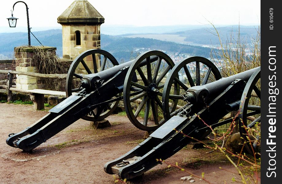 Two old cannons are standing on a court of a castle.