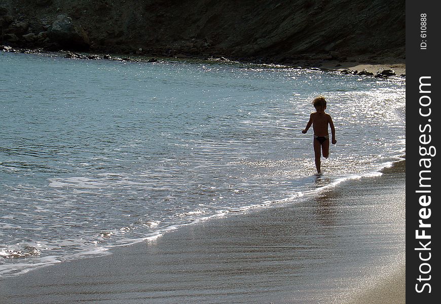 A small child running on tha beach break. In the summer time, a small child running on the wave. A small child running on tha beach break. In the summer time, a small child running on the wave.