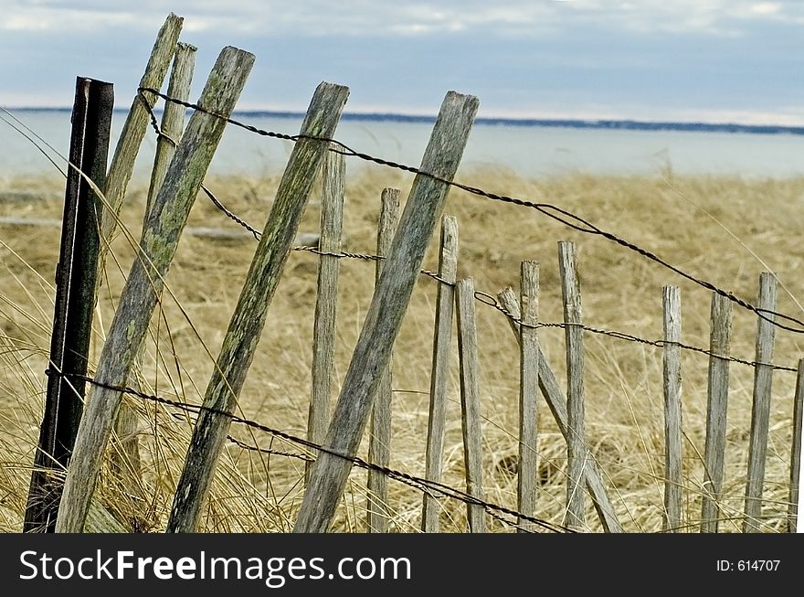 A weathered wooden and wire fence on a sand dune on a Maine beach. A weathered wooden and wire fence on a sand dune on a Maine beach.