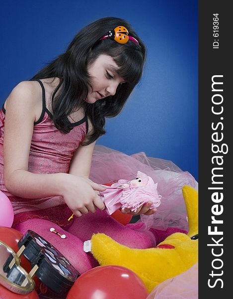 Young and beautiful girl playing with her doll, surrounded by balloons and make up kit