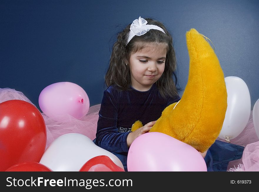 Sweet young girl playing with her plush moon surrounded by coloured balloons