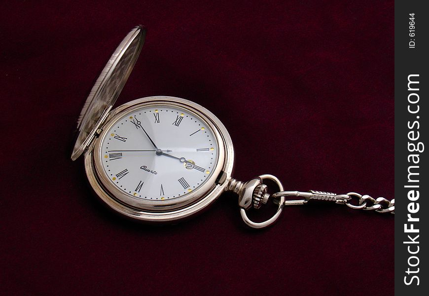 Open silver pocket watch with a chain on purple silk background