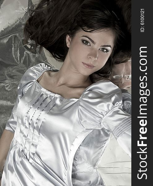 A beautiful young girl lies on a brilliant background in silver clothes. A beautiful young girl lies on a brilliant background in silver clothes