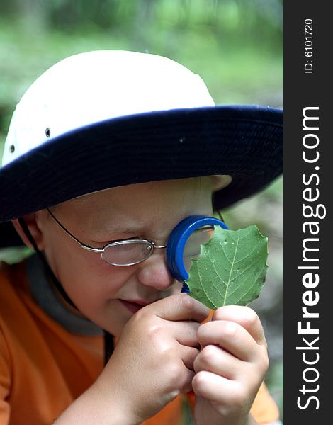 Young boy studying leaf through magnifying glass