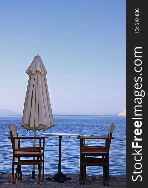 Two empty wooden chairs on the edge of the ocean (Greek islands). Two empty wooden chairs on the edge of the ocean (Greek islands).