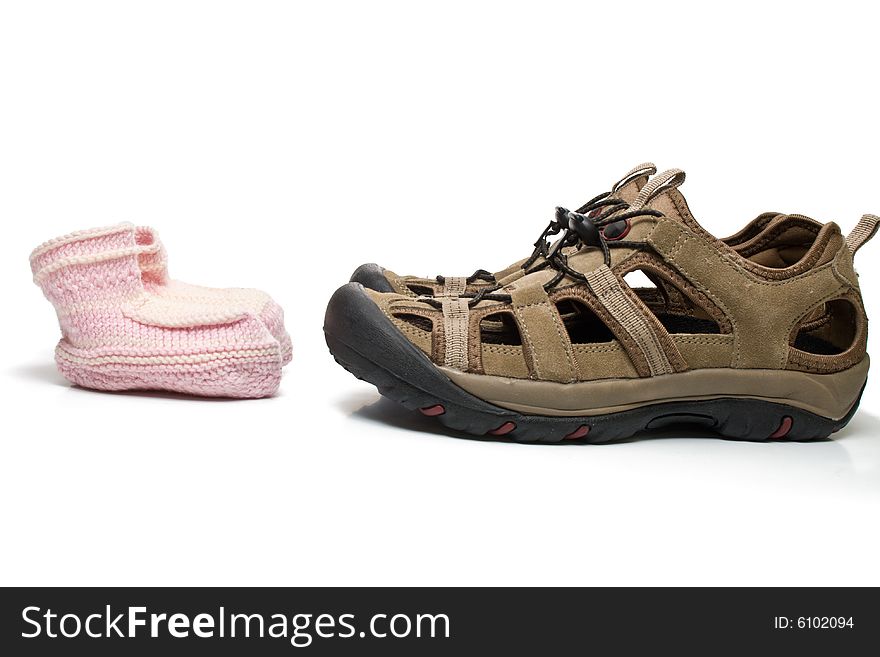 Pink baby bootees standing opposite large male shoes, isolated, on white background. Pink baby bootees standing opposite large male shoes, isolated, on white background