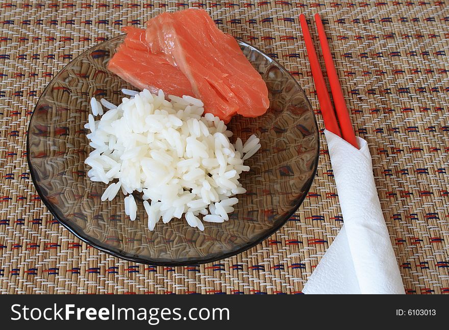 Boiled rice and fish on glassy plate and red chopsticks