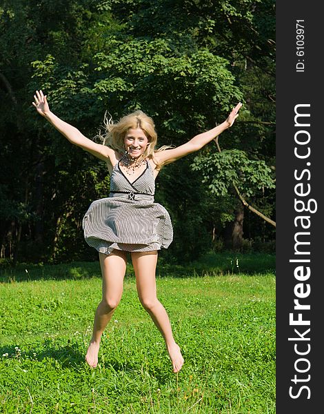Girl in a summer dress jumps on a green grass on a background of trees. Girl in a summer dress jumps on a green grass on a background of trees