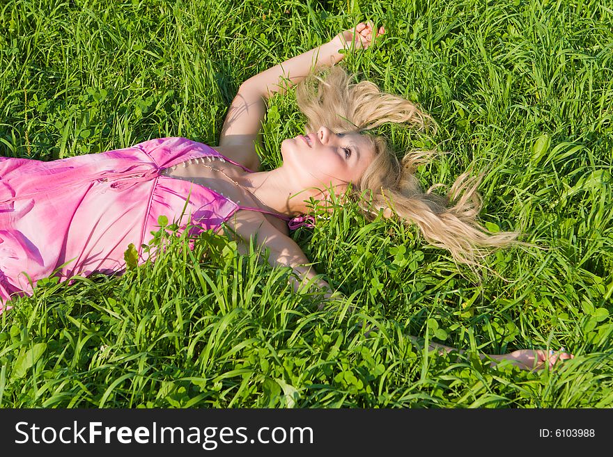 Girl in a pink summer dress has a rest on a green grass. Girl in a pink summer dress has a rest on a green grass