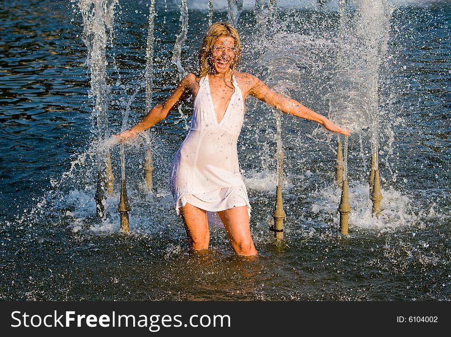 Beautiful girl in a white dress laps in jets of a fountain. Beautiful girl in a white dress laps in jets of a fountain