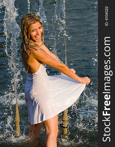 Beautiful girl in a white dress laps in jets of a fountain. Beautiful girl in a white dress laps in jets of a fountain