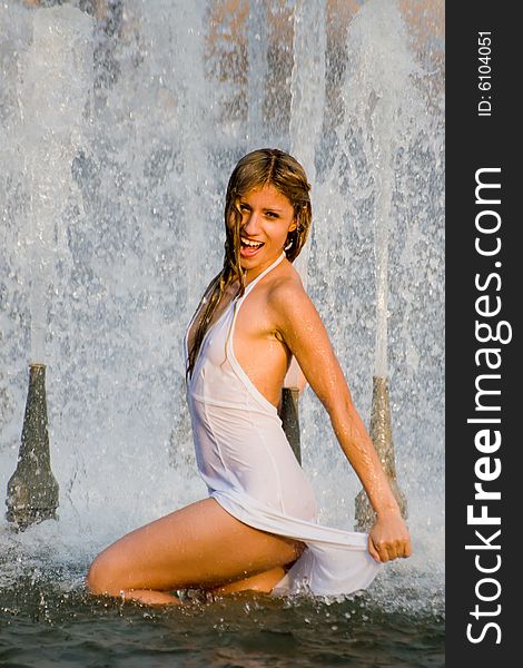 Beautiful girl in a white dress laps in jets of a fountain. Beautiful girl in a white dress laps in jets of a fountain