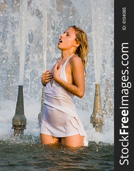 Beautiful girl in a white dress laps in jets of a fountain. Beautiful girl in a white dress laps in jets of a fountain