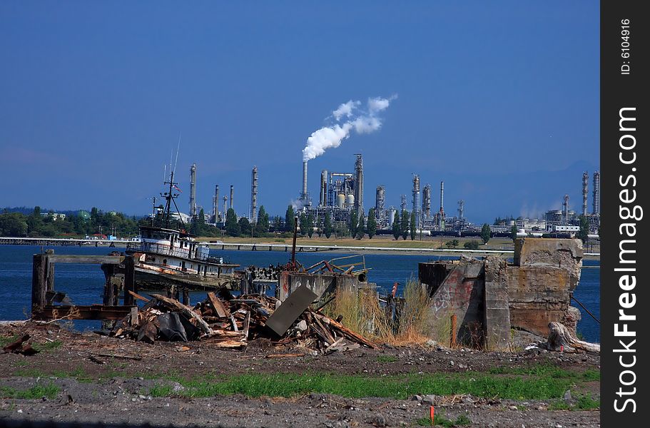 View of an oil refinery from a dock area across the bay, with trash and vandalism in the foreground.