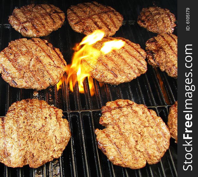 Cooking hamburgers on a grill with flames.