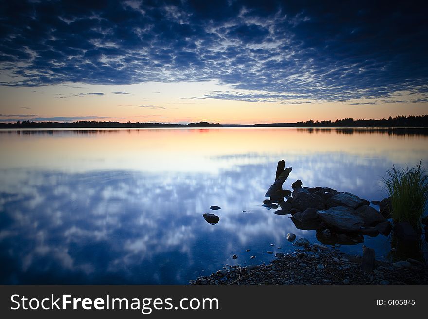 Sunset on rocky beach with cloud reflections