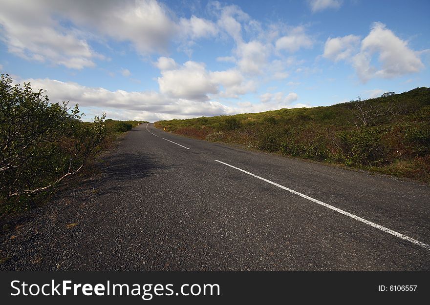 Sunlit road disappearing into the distance under the partially cloudy sky.