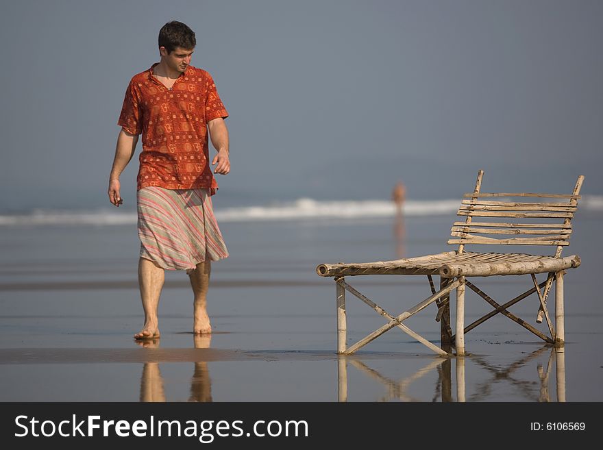 Man is walking on the the beach near a trestle-bed. Man is walking on the the beach near a trestle-bed