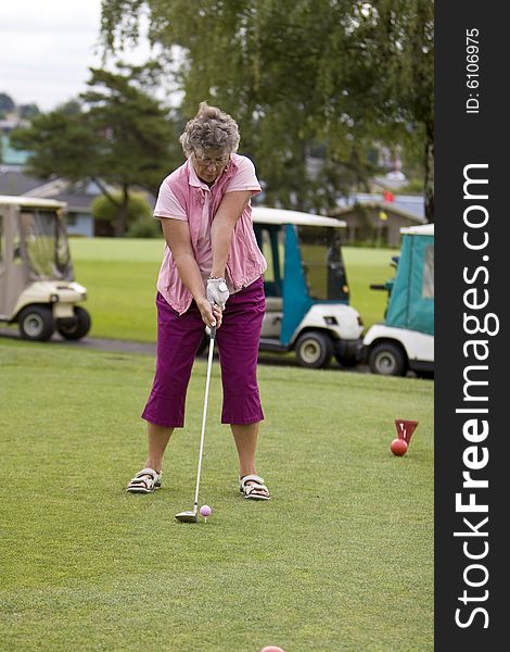 Elderly woman teeing off with golf carts in the background. Vertically framed photo. Elderly woman teeing off with golf carts in the background. Vertically framed photo.