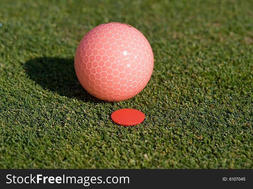 Pink golfball rests on green next to golfball marker. Horizontally framed photo. Pink golfball rests on green next to golfball marker. Horizontally framed photo.