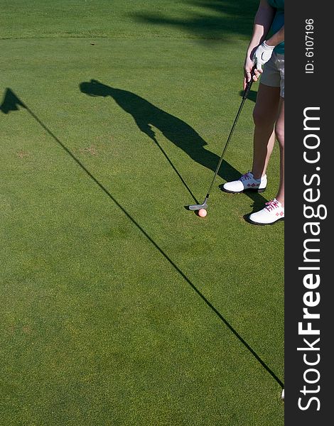 Golfer's shadow shows him putting on golf green. Vertically framed photo. Golfer's shadow shows him putting on golf green. Vertically framed photo.