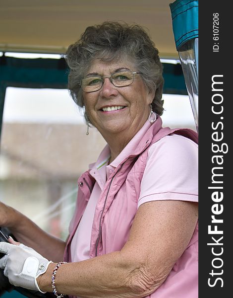 Elderly woman with golf glove smiling as she rides in a golf cart. Vertically framed photo. Elderly woman with golf glove smiling as she rides in a golf cart. Vertically framed photo.