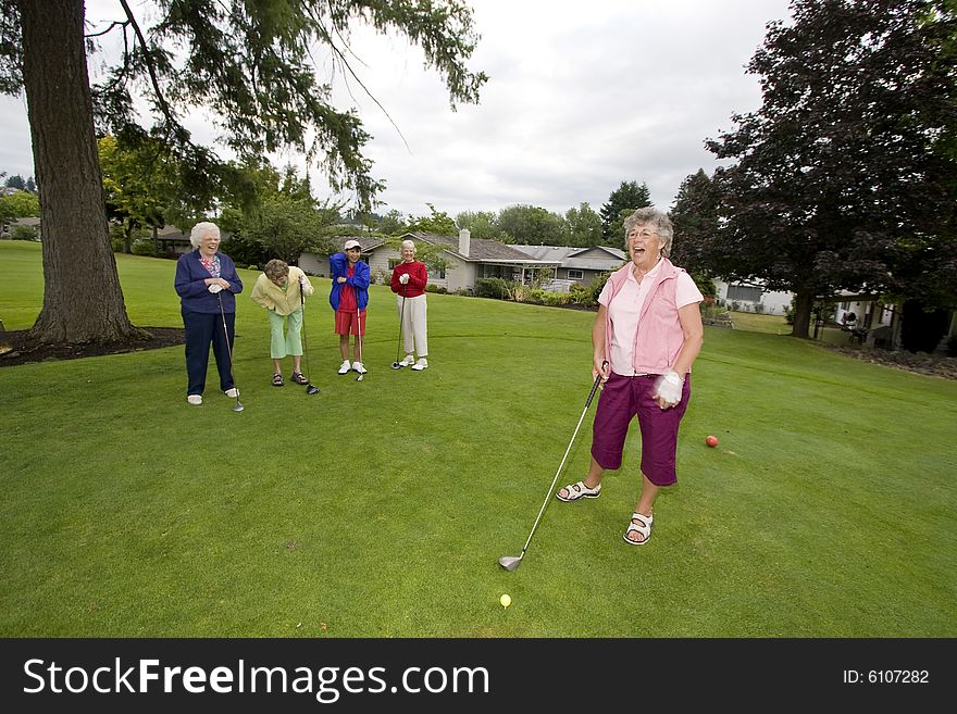 Five elderly women playing golf and laughing. Horizontally framed photo.