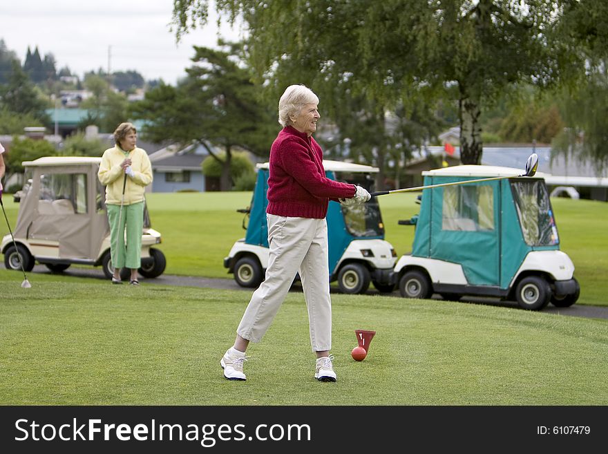 Two women golfing, one is teeing off. Horizontally framed photo. Two women golfing, one is teeing off. Horizontally framed photo.