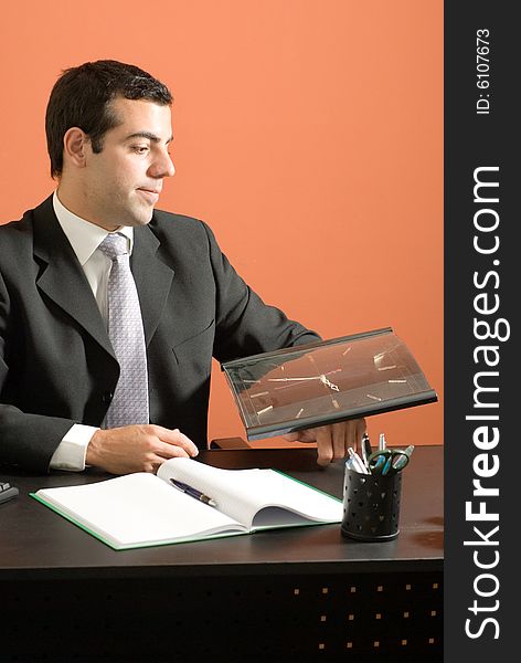 Business man smiles as he sits at his desk looking at his clock. Vertically framed photo. Business man smiles as he sits at his desk looking at his clock. Vertically framed photo.