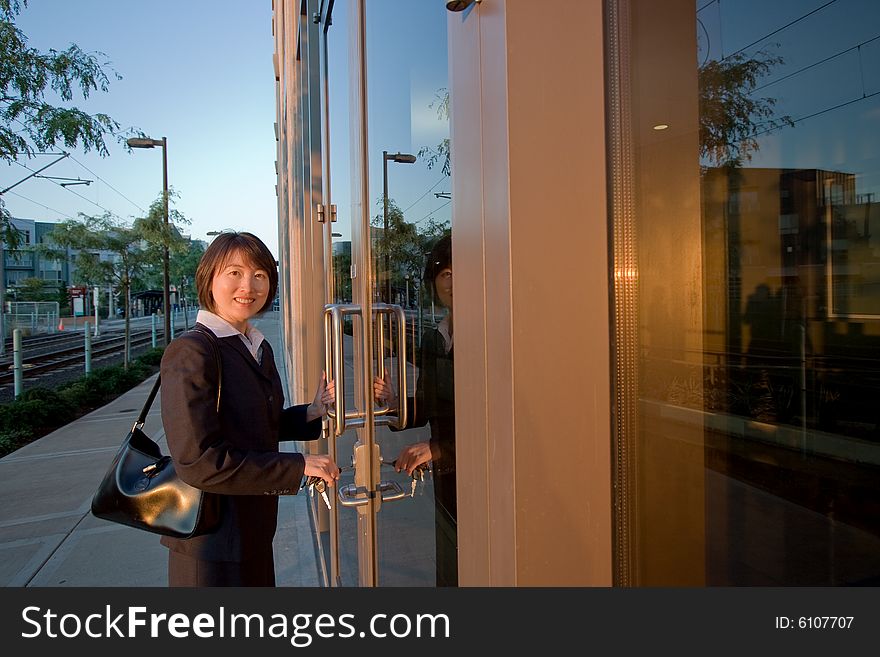 Woman wearing suit smiles at camera while opening door. She has a purse over her shoulder. Horizontally framed photo. Woman wearing suit smiles at camera while opening door. She has a purse over her shoulder. Horizontally framed photo.