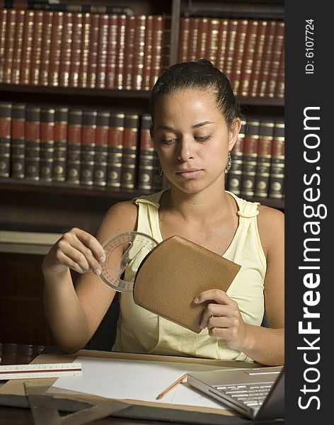 Woman seated in library puts a protractor away in its case. There are books behind her and she is seated at a table. Vertically framed photo. Woman seated in library puts a protractor away in its case. There are books behind her and she is seated at a table. Vertically framed photo.