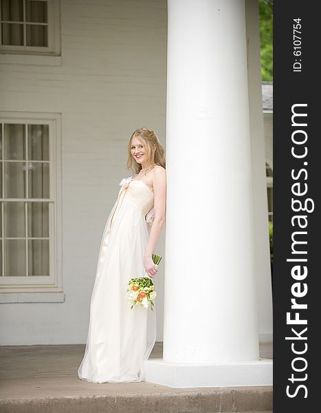 An image of a smiling bride leaning on a large column