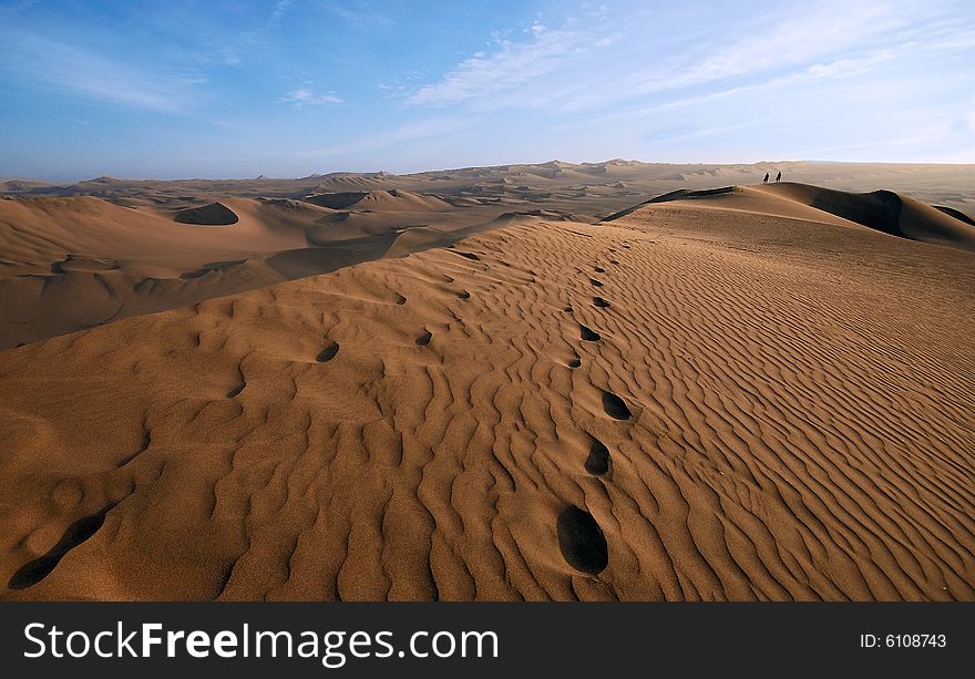 Men walking in the midlle of a huge sand dune