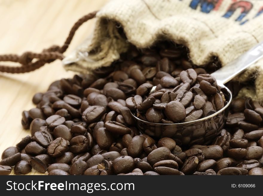 Coffee beans spilling out of burlap sack with stainless steel measuring scoop.