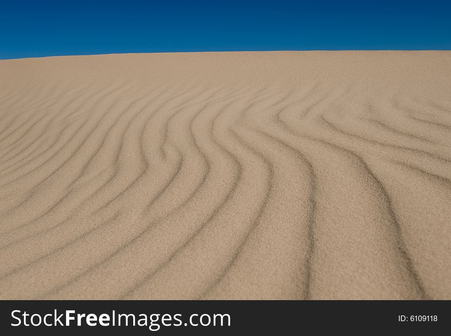 A image of a rolling sand dunes on a bright blue sky
