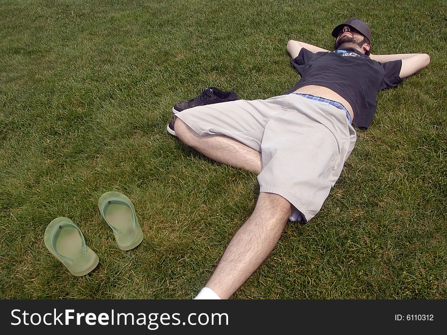 A man with a hat over his head resting in the grass. A man with a hat over his head resting in the grass.