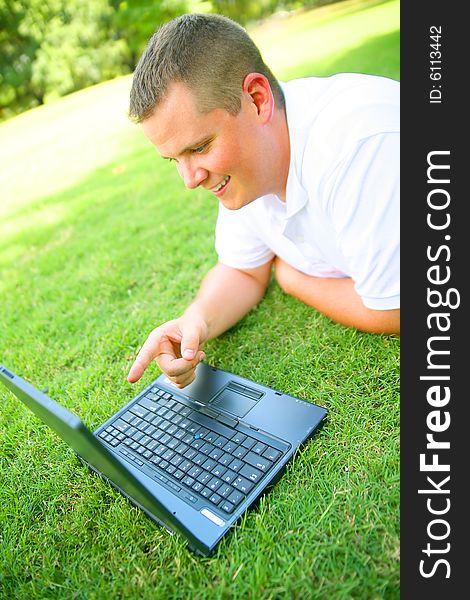 Handsome caucasian man using computer outdoor in grassy park. Handsome caucasian man using computer outdoor in grassy park