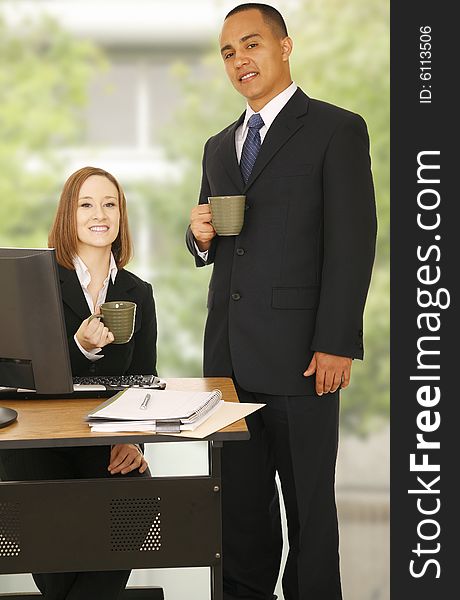 Two business people, one standing and the other sitting. both look at camera and smile. concept for business team, office break or team work. Two business people, one standing and the other sitting. both look at camera and smile. concept for business team, office break or team work