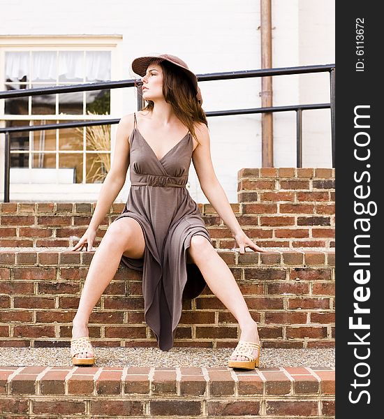 Beautiful woman wearing a brown dress and matching hat sitting on brick stairs