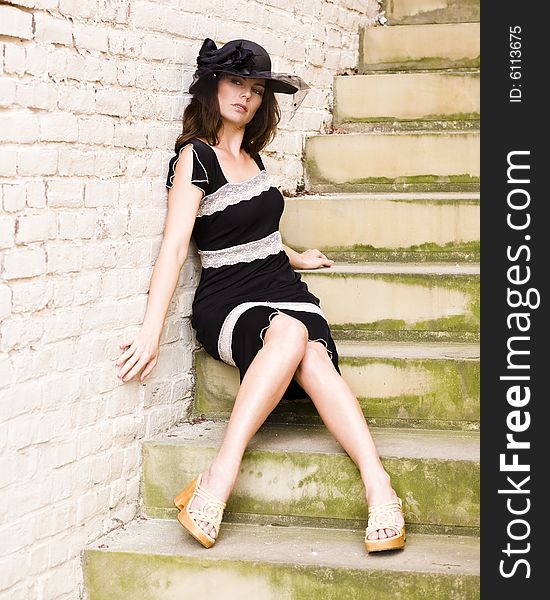 Beautiful woman wearing a black dress and hat sitting on stone stairs