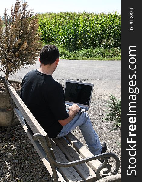 The man sitting on a bench using his laptop. The man sitting on a bench using his laptop