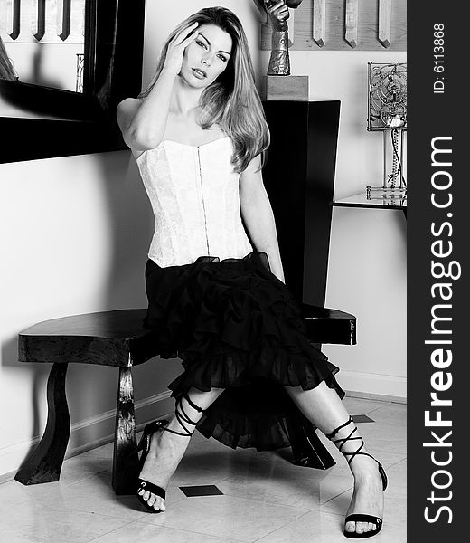 Beautiful woman wearing white corset and black skirt sitting on an art deco style bench