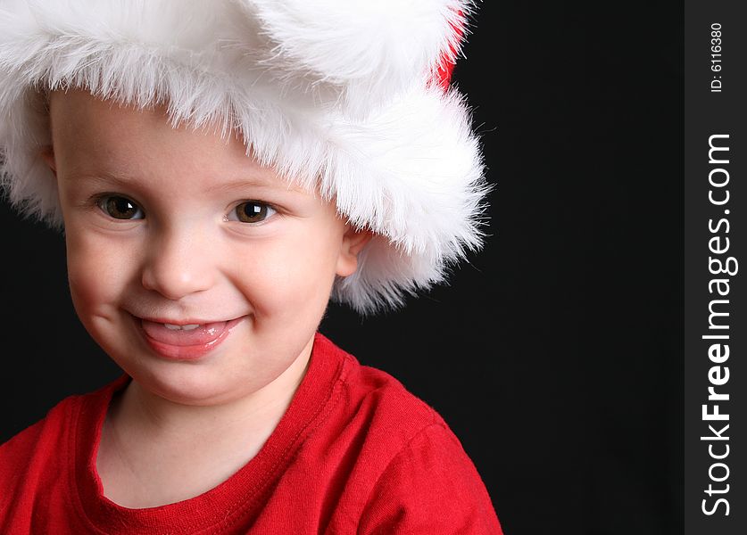 Blonde toddler against a black background wearing a christmas hat