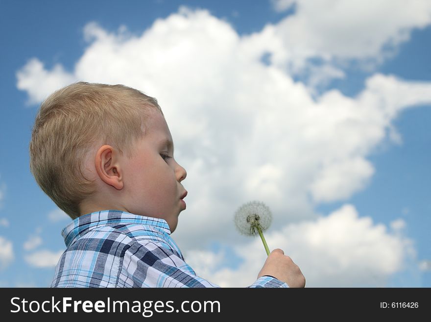 Boy blowing dandelion over blue sky