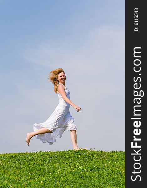 Girl runs on a grass on a background of the blue sky