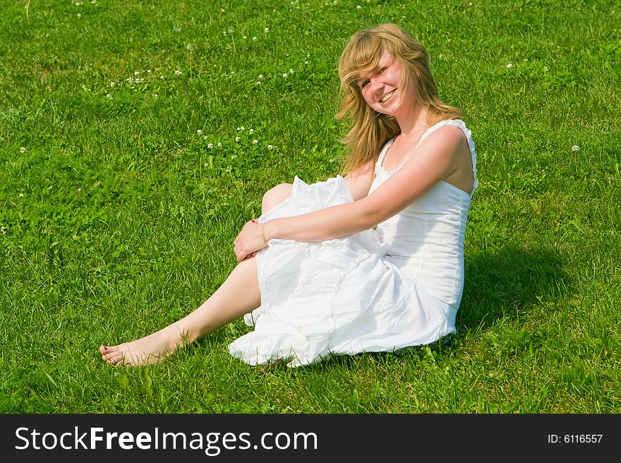 Girl in a white dress sits on a green grass. Girl in a white dress sits on a green grass