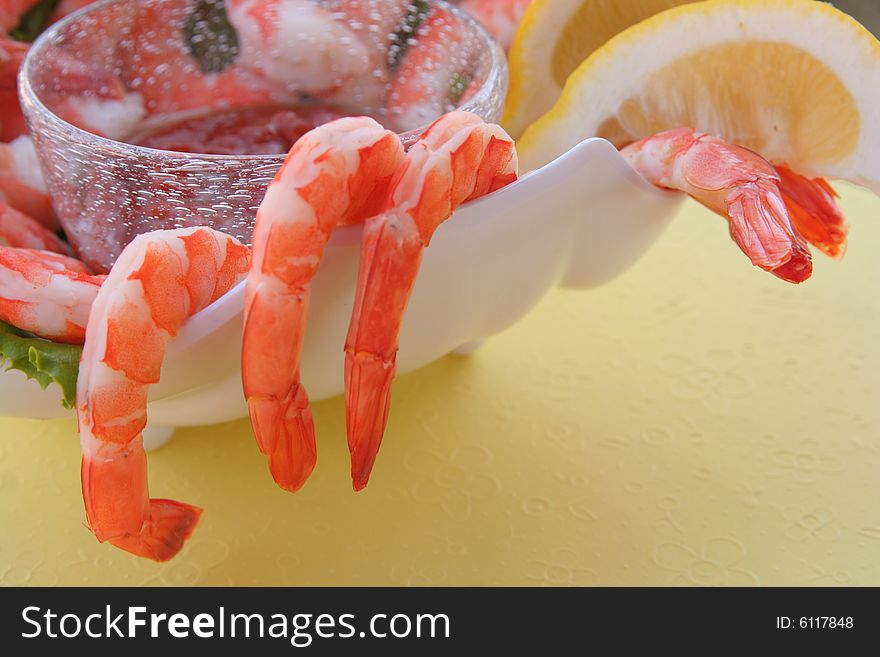 Bowl of chilled shrimp cocktail with lemon wedges on a soft yellow background. Bowl of chilled shrimp cocktail with lemon wedges on a soft yellow background.