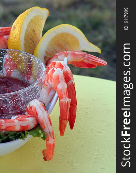 Bowl of chilled shrimp cocktail with lemon wedges on a soft yellow background, served outdoors. Bowl of chilled shrimp cocktail with lemon wedges on a soft yellow background, served outdoors.