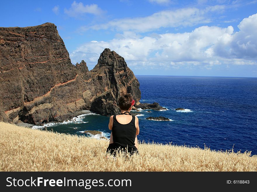 Girl sitting in arid grass and staring at the ocean on the peninsula Sao Lourenco, Madeira. Girl sitting in arid grass and staring at the ocean on the peninsula Sao Lourenco, Madeira.