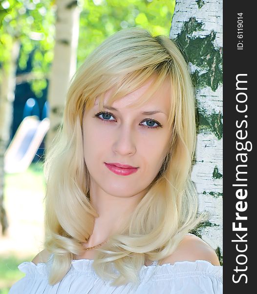 Portrait of pretty blonde girl near of birch stem